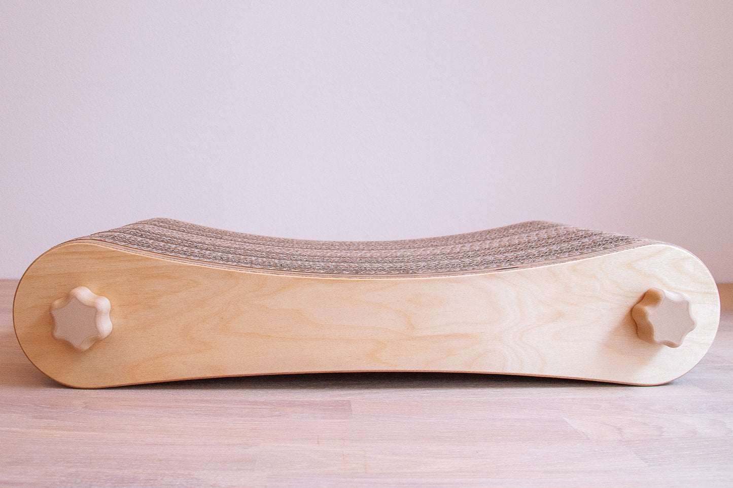 Kratzmöbel für Katzen in Form einer Liege bestehend aus zwei hellen Holzelementen mit Wellpappebögen dazwischen. Die Verschraubung erfolgt mit Muttern aus Holzfilament in Form von abgerundeten Sternen.