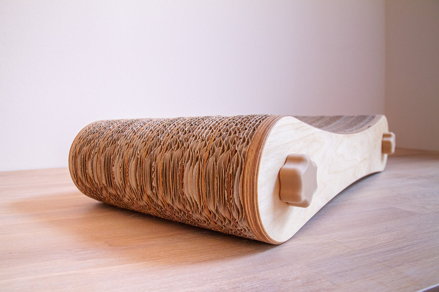 Kratzmöbel für Katzen in Form einer Liege bestehend aus zwei hellen Holzelementen mit Wellpappebögen dazwischen. Die Verschraubung erfolgt mit Muttern aus Holzfilament in Form von abgerundeten Sternen.