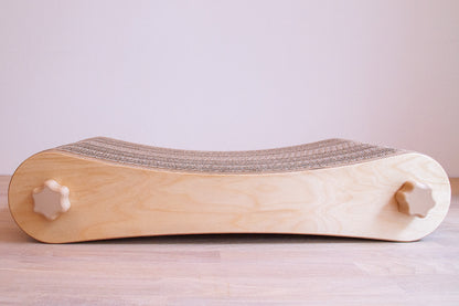 Kratzmöbel für Katzen in Form einer Liege bestehend aus zwei hellen Holzelementen mit Wellpappebögen dazwischen. Die Verschraubung erfolgt mit Muttern aus Holzfilament in Form von abgerundeten Sternen.
