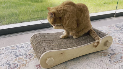 Kratzmöbel für Katzen in Form einer Liege bestehend aus zwei hellen Holzelementen mit Wellpappebögen dazwischen. Die Verschraubung erfolgt mit Muttern aus Holzfilament in Form von abgerundeten Sternen. Mittelgroße rot-getigerte Katze, ca. 4 kg betreibt Fellpflege auf der Liege, um die Größe in Relation zur Katze darzustellen.